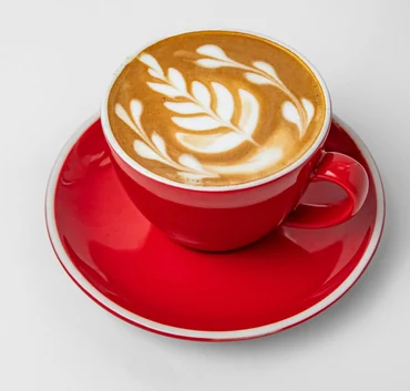 Cortado with leaf latte art in a red cup and saucer