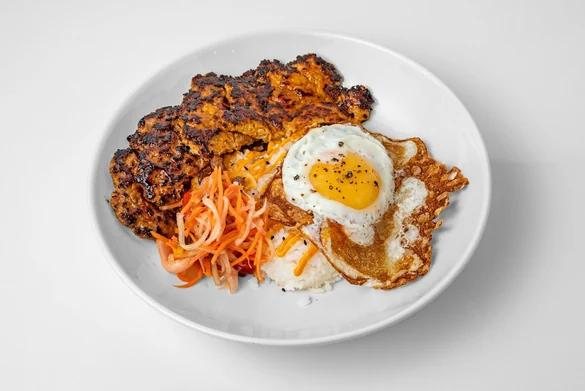 Breakfast rice bowl with a charred sausage patty, a fried egg, pickled papaya and steamed rice in a white bowl