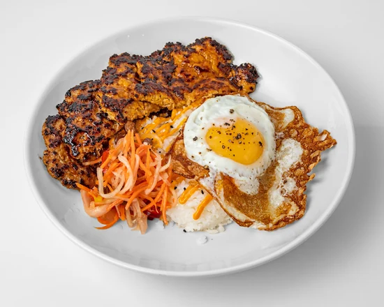 Breakfast rice bowl with a charred sausage patty, a fried egg, pickled papaya and steamed rice in a white bowl
