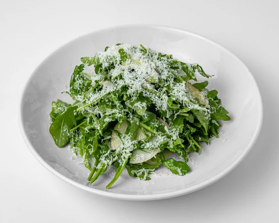 Arugula salad with sliced Asian pear and grated cheese in a white bowl